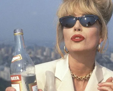 Woman with blond hair in sunglasses, red lipstick, white suit holding a bottle.