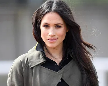 A woman with long dark hair wearing a green trench coat and black top, looking to the side.