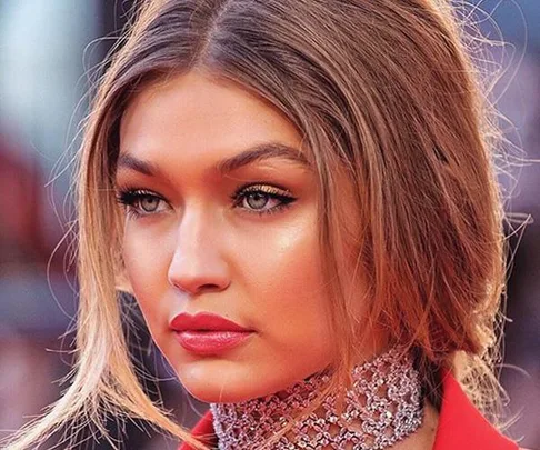 Close-up of Gigi Hadid with natural makeup, glossy lips, and styled hair, wearing a sparkly choker necklace.