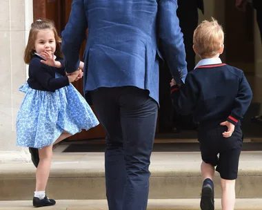 Man in blue suit holding hands with a young girl and boy, walking up steps. The girl wears a blue dress, the boy wears a dark outfit.