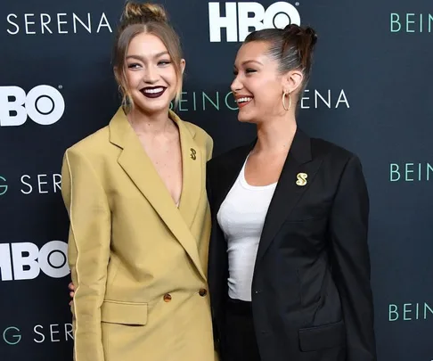 Gigi and Bella Hadid smiling in matching pantsuits at HBO's "Being Serena" premiere.