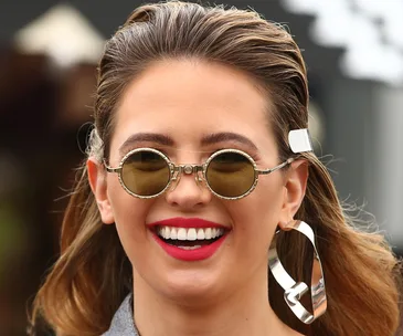 Woman smiling in round sunglasses and bold earrings.