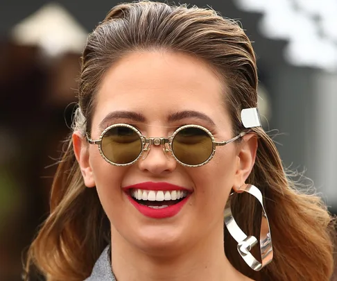 Woman smiling in round sunglasses and bold earrings.