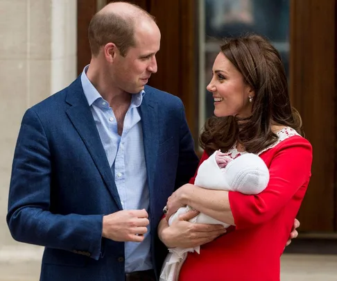 A couple smiling at each other while the woman holds a newborn baby wrapped in a white blanket.