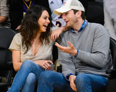 A couple sitting courtside at a basketball game, smiling and chatting with each other.