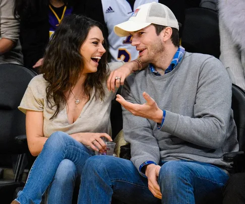 A couple sitting courtside at a basketball game, smiling and chatting with each other.