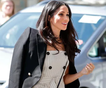 Meghan Markle in a striped dress and blazer, smiles while standing outside near a car at the Commonwealth Heads of Government Meeting.