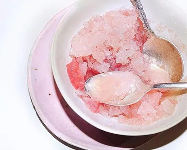 A bowl of pink granita with two spoons. The bowl rests on a pink plate.