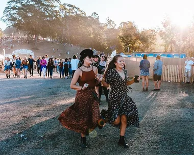 Festival-goers walking and smiling at Splendour in the Grass 2018, surrounded by crowds and trees in the background.