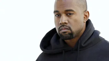 A man with a short buzz cut, beard, and mustache wearing a black hoodie gazes intently at the camera.