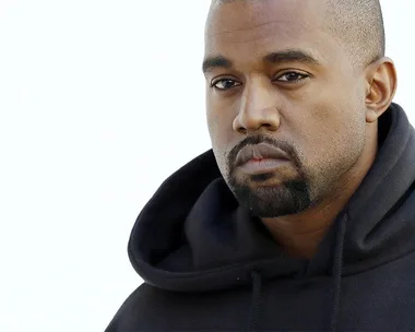 A man with a short buzz cut, beard, and mustache wearing a black hoodie gazes intently at the camera.