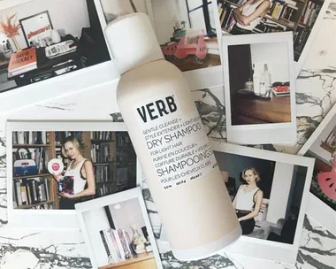 Bottle of Verb dry shampoo on a marble surface surrounded by several polaroid photos.