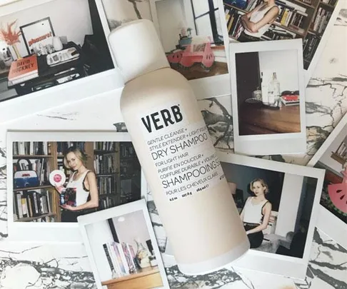 Bottle of Verb dry shampoo on a marble surface surrounded by several polaroid photos.