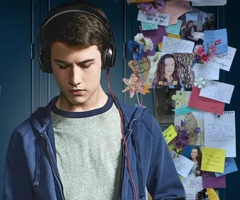 Teenage boy wearing headphones, standing in front of a locker with notes, photos, and flowers from "13 Reasons Why".