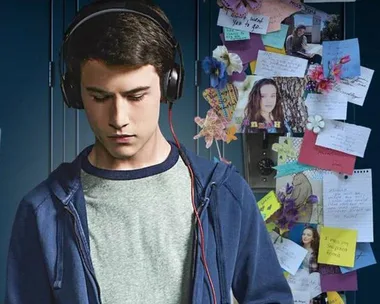 Teenage boy wearing headphones, standing in front of a locker with notes, photos, and flowers from "13 Reasons Why".