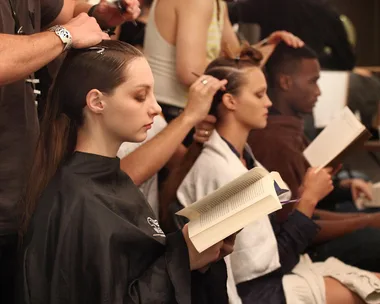 People reading books while getting their hair styled backstage.