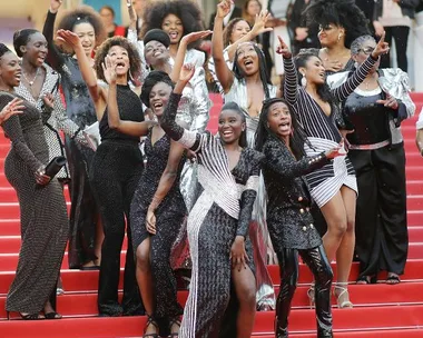 A group of Black actresses in glamorous outfits pose energetically on the red carpet at Cannes Film Festival.