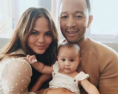 Chrissy Teigen and John Legend smile while holding their baby, Miles Theodore Stephens, for a family photo at home.