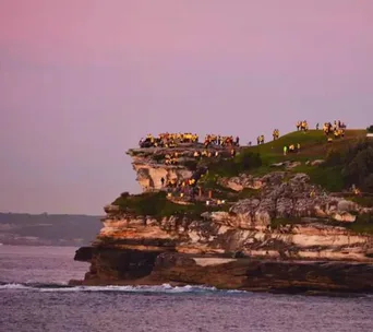 People gather on a cliff overlooking the ocean at sunrise during the Darkness Into Light walk event.