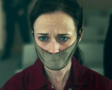 Emily from The Handmaid’s Tale looks forward, gagged, with a distressed expression in a dystopian setting.