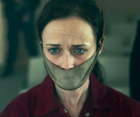 Emily from The Handmaid’s Tale looks forward, gagged, with a distressed expression in a dystopian setting.