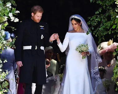 Prince Harry and Meghan Markle exiting the chapel after their royal wedding, Meghan wearing a white dress and veil, holding flowers.