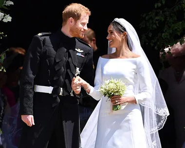 Bride and groom holding hands and smiling at each other outside, bride in white dress and veil, groom in military uniform.