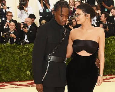 Kylie Jenner and Travis Scott in black outfits, pose together at the Met Gala with photographers in the background.