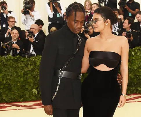 Kylie Jenner and Travis Scott in black outfits, pose together at the Met Gala with photographers in the background.