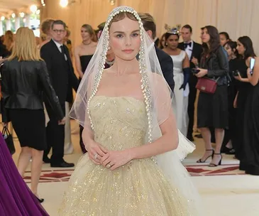 A woman in a sparkling strapless gown with a pearl-edged veil at the Met Gala 2018, surrounded by a crowd.