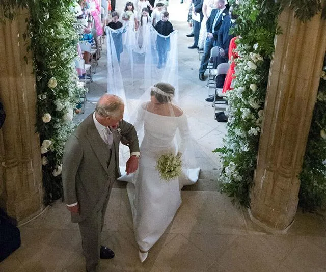 The bride walks down the aisle with an older man in a suit at a wedding ceremony, followed by flower girls and boys.