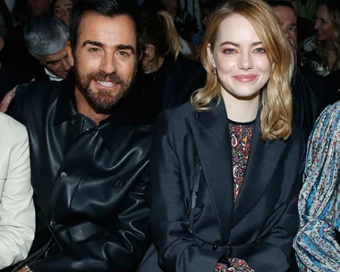 A man in a black leather jacket and a woman in a dark blazer sit closely together and smile at an event.