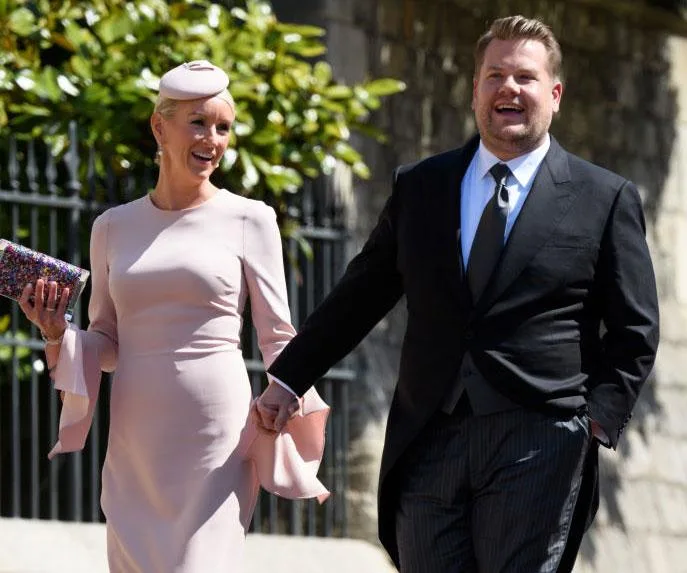 James Corden and his wife Julia Carey holding hands and smiling at Prince Harry and Meghan Markle's wedding.