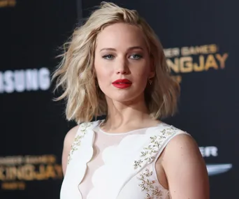 Woman with short blonde hair and red lipstick in a white dress at a "Mockingjay" movie premiere.