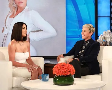 Kim Kardashian being interviewed by Ellen DeGeneres on set, with a photo of Khloe Kardashian in the background.