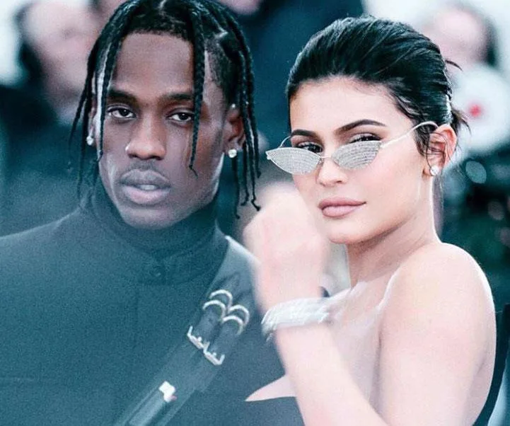 Kylie Jenner and Travis Scott at a public event, Kylie wearing sunglasses and an elegant dress.