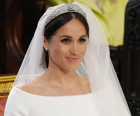 A bride in a white dress and veil, wearing a diamond tiara, smiling softly.