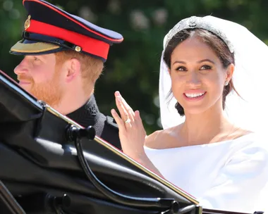 Prince Harry in uniform and Meghan Markle in wedding dress smile and wave from a carriage at their royal wedding.