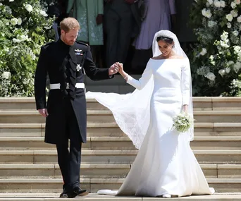 Bride and groom in formal attire holding hands, descending steps with floral decoration. Bride in white dress holding bouquet.