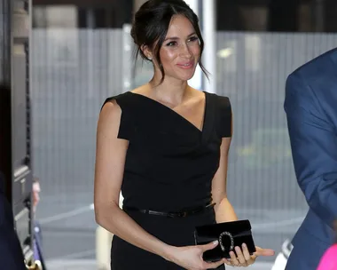 Woman in a black dress holding a black clutch and smiling at an indoor event.