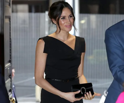 Woman in a black dress holding a black clutch and smiling at an indoor event.