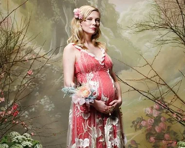 Pregnant woman in a floral dress posing in front of a whimsical, nature-themed backdrop.