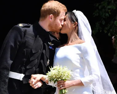 Bride and groom kiss at their royal wedding, the bride in a white gown with a bouquet.