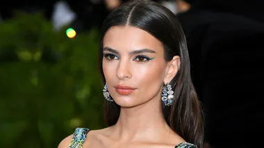 A woman with long brown hair, wearing a colorful dress and statement earrings at the 2018 Met Gala.