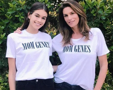 Two women wearing matching "MOM GENES" shirts standing together outdoors, smiling.