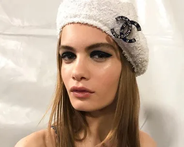 Woman wearing a white beret with a Chanel logo, displaying easy cat-eye makeup.