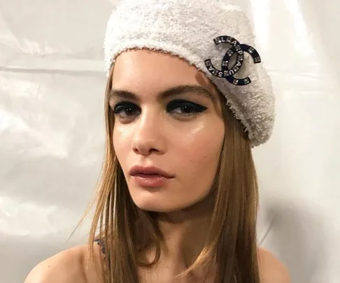 Woman wearing a white beret with a Chanel logo, displaying easy cat-eye makeup.