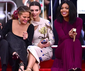 Three women seated at the Met Gala, smiling and interacting with each other, dressed in elegant gowns.