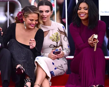 Three women seated at the Met Gala, smiling and interacting with each other, dressed in elegant gowns.