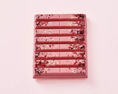 A pink ruby chocolate bar with berry pieces embedded in it, displayed against a light pink background.